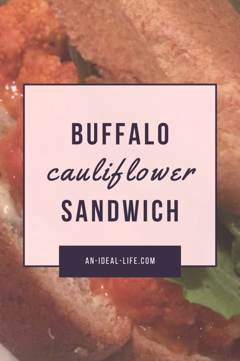 A close-up food graphic showing a buffalo cauliflower sandwich in the background, with visible cauliflower coated in orange buffalo sauce and green lettuce. Centered over the image is a pale pink text box outlined in dark purple that reads: “Buffalo Cauliflower Sandwich.” At the bottom of the box, the website an-ideal-life.com is displayed.