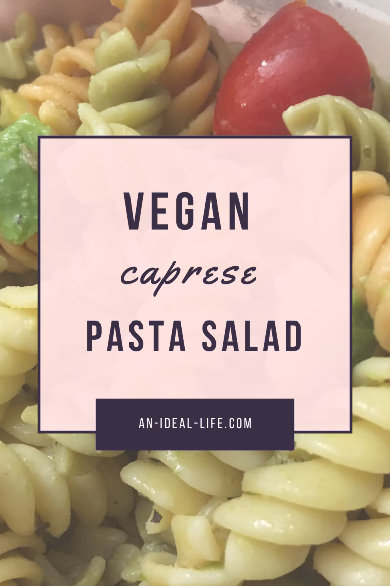 A close-up image of tri-color rotini pasta with avocado chunks and cherry tomatoes, overlaid with a semi-transparent text box. The text reads: “Vegan Caprese Pasta Salad” with the website an-ideal-life.com listed at the bottom. The background suggests a fresh, chilled pasta dish without dairy, aligning with the vegan theme.