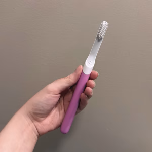 A person's hand holding a quip electric toothbrush with a pink handle and white bristles.